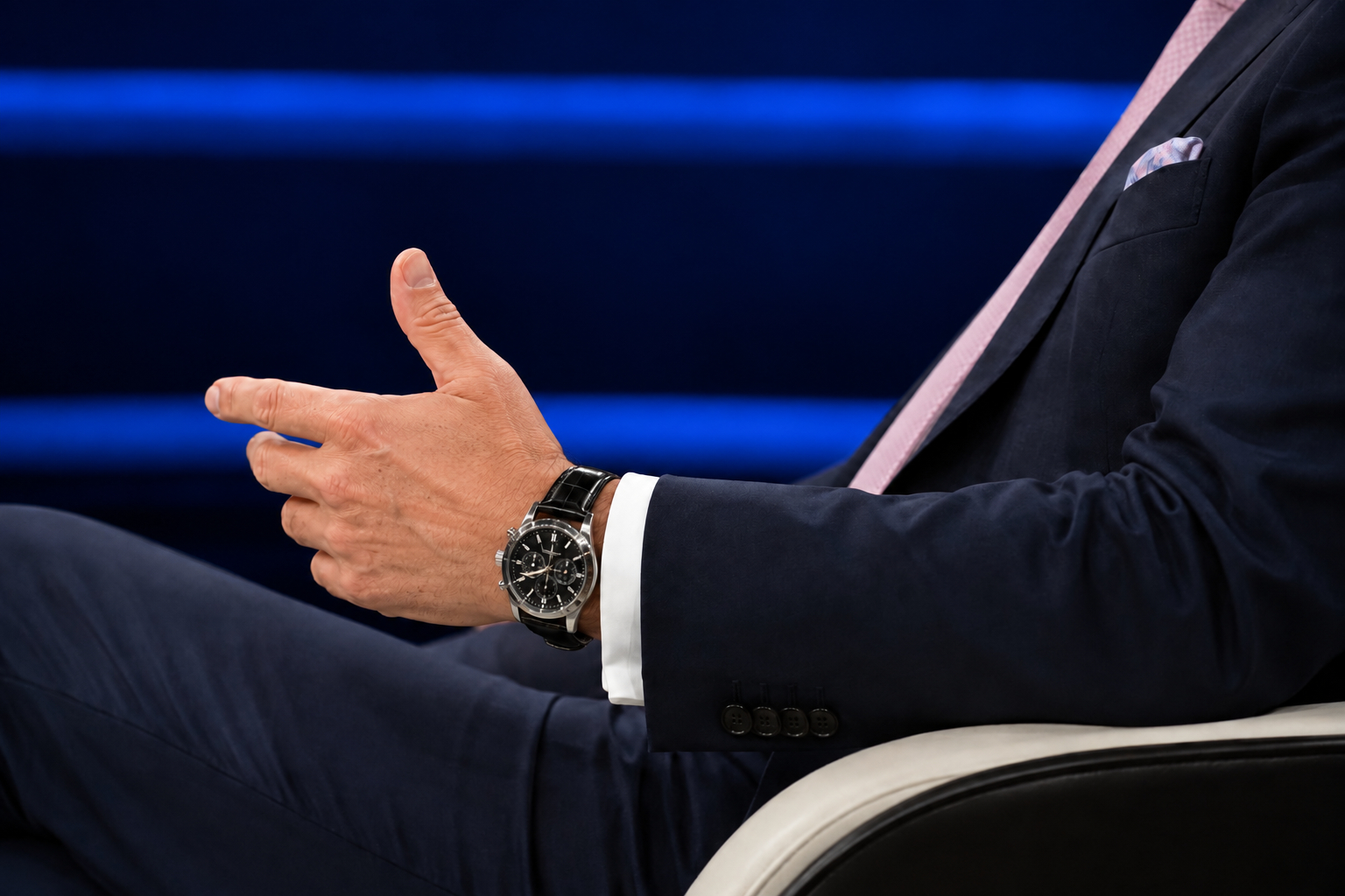 Homme en costume bleu nuit portant un chronographe acier au poignet dans un studio de télévision